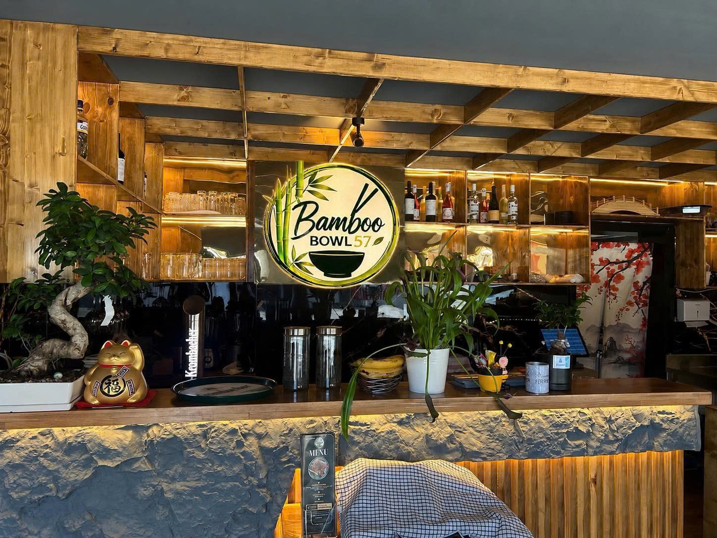 Der Empfangsbereich von Bamboo Bowl 57 mit Bambusholz und beleuchtetem Restaurantlogo